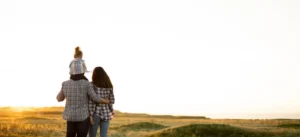 Family with a young child on a parent's shoulders watching the sunset over open fields