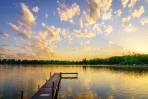 Wooden dock on a calm lake at sunset beneath a sky of scattered clouds
