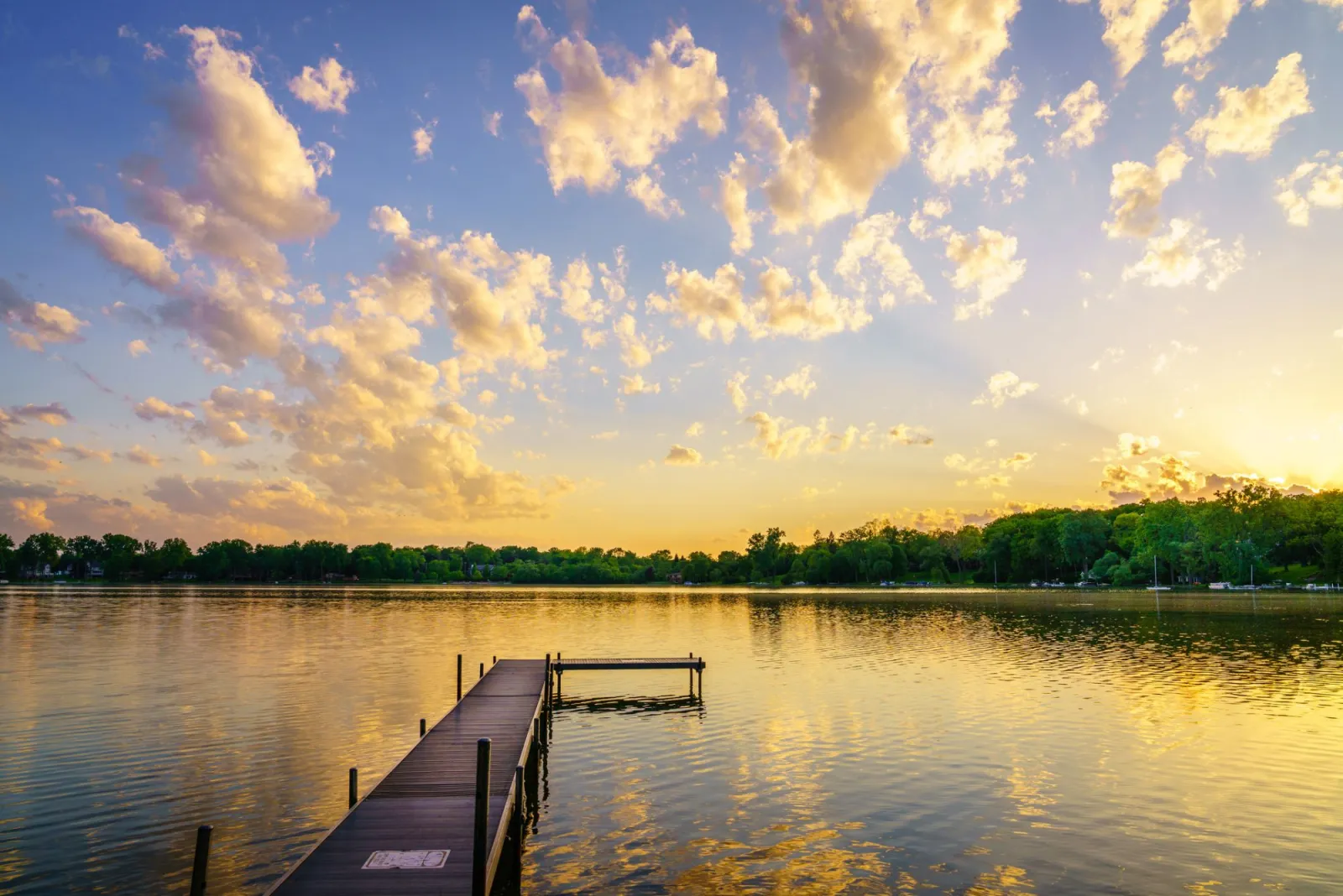 Wooden dock on a calm lake at sunset beneath a sky of scattered clouds